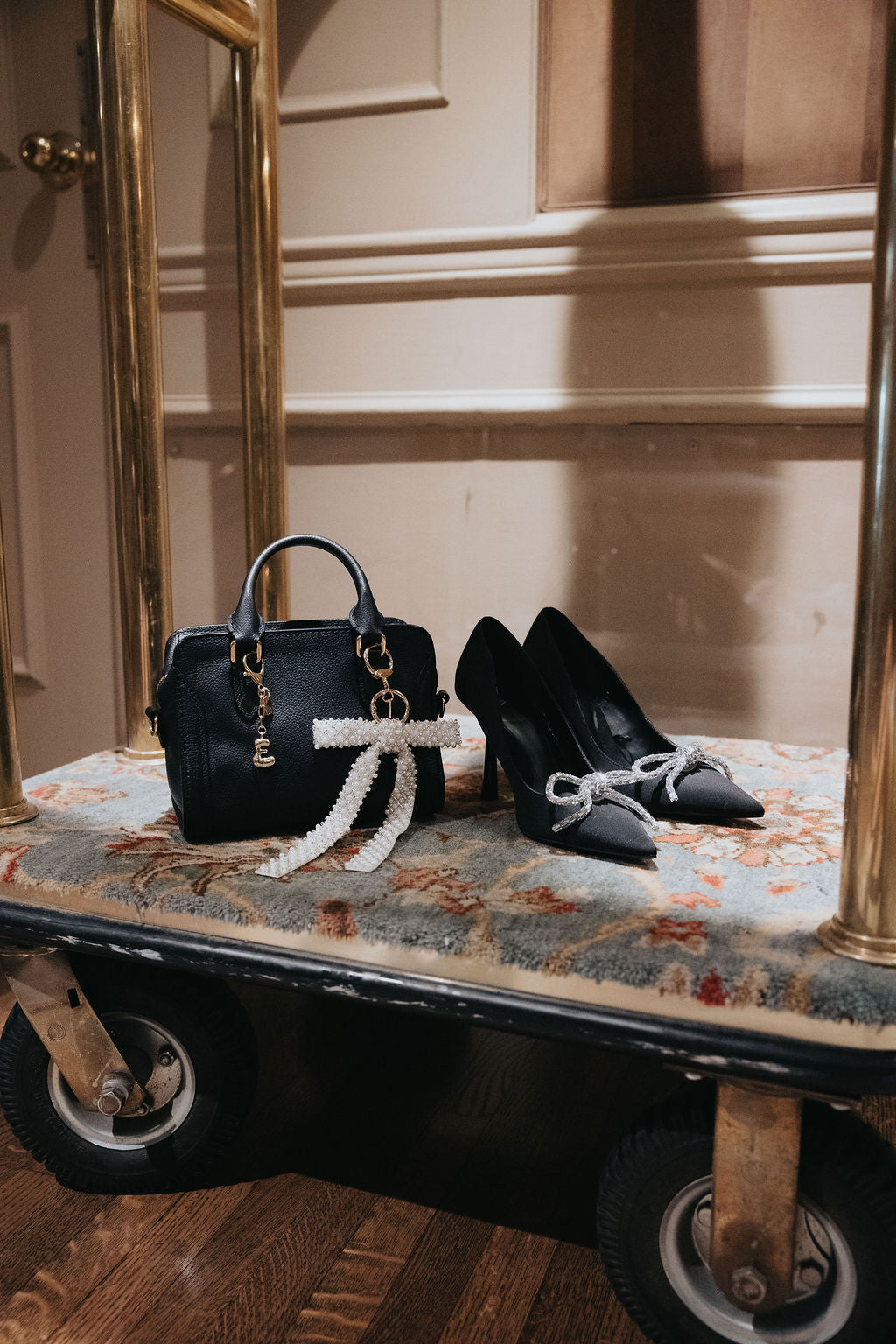 Purse Charms on Black handbag and high heels on a vintage suitcase with ornate wall and floor in the background