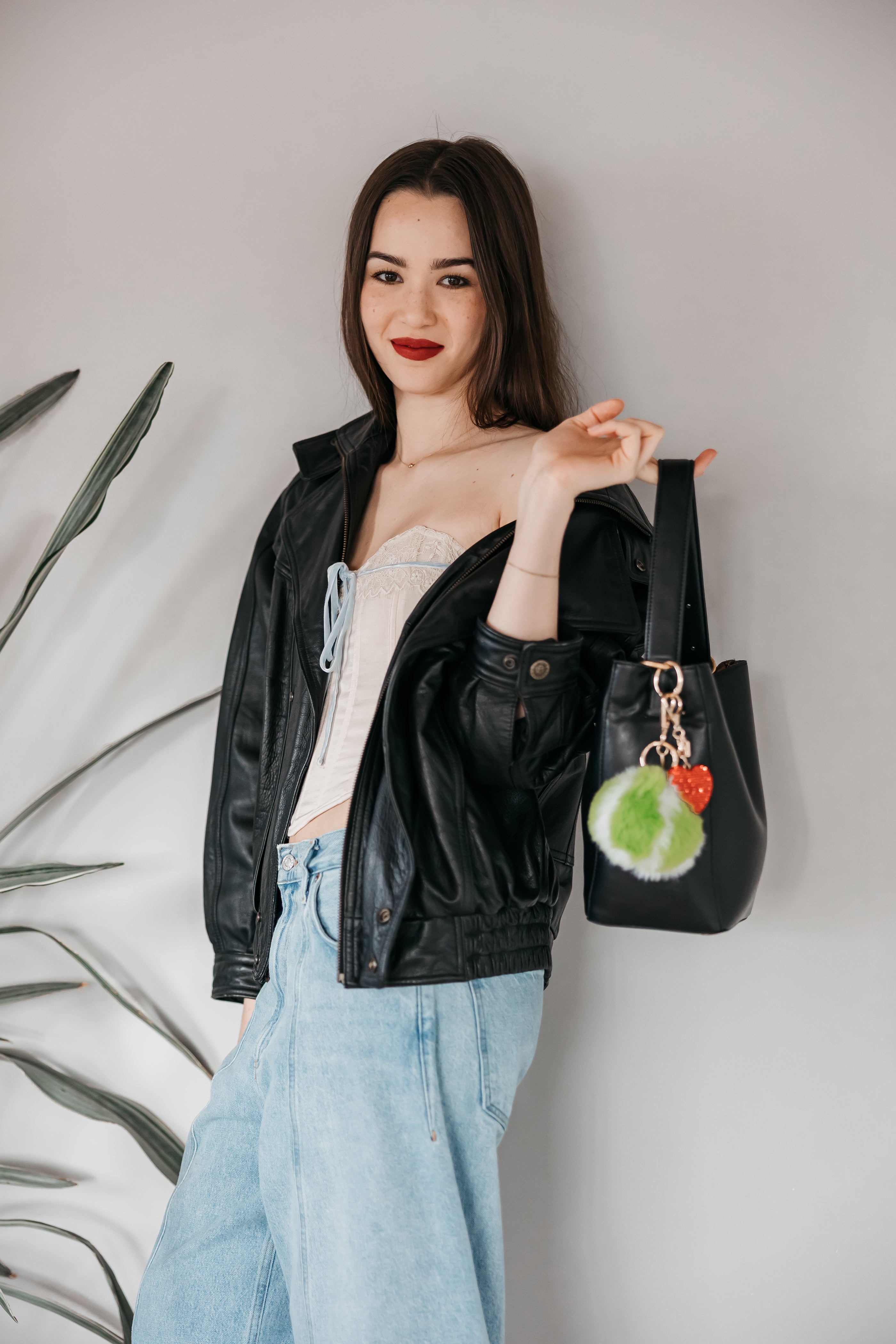 Woman holding a black handbag with a tennis pom charm. Red Sparky Heart Charm