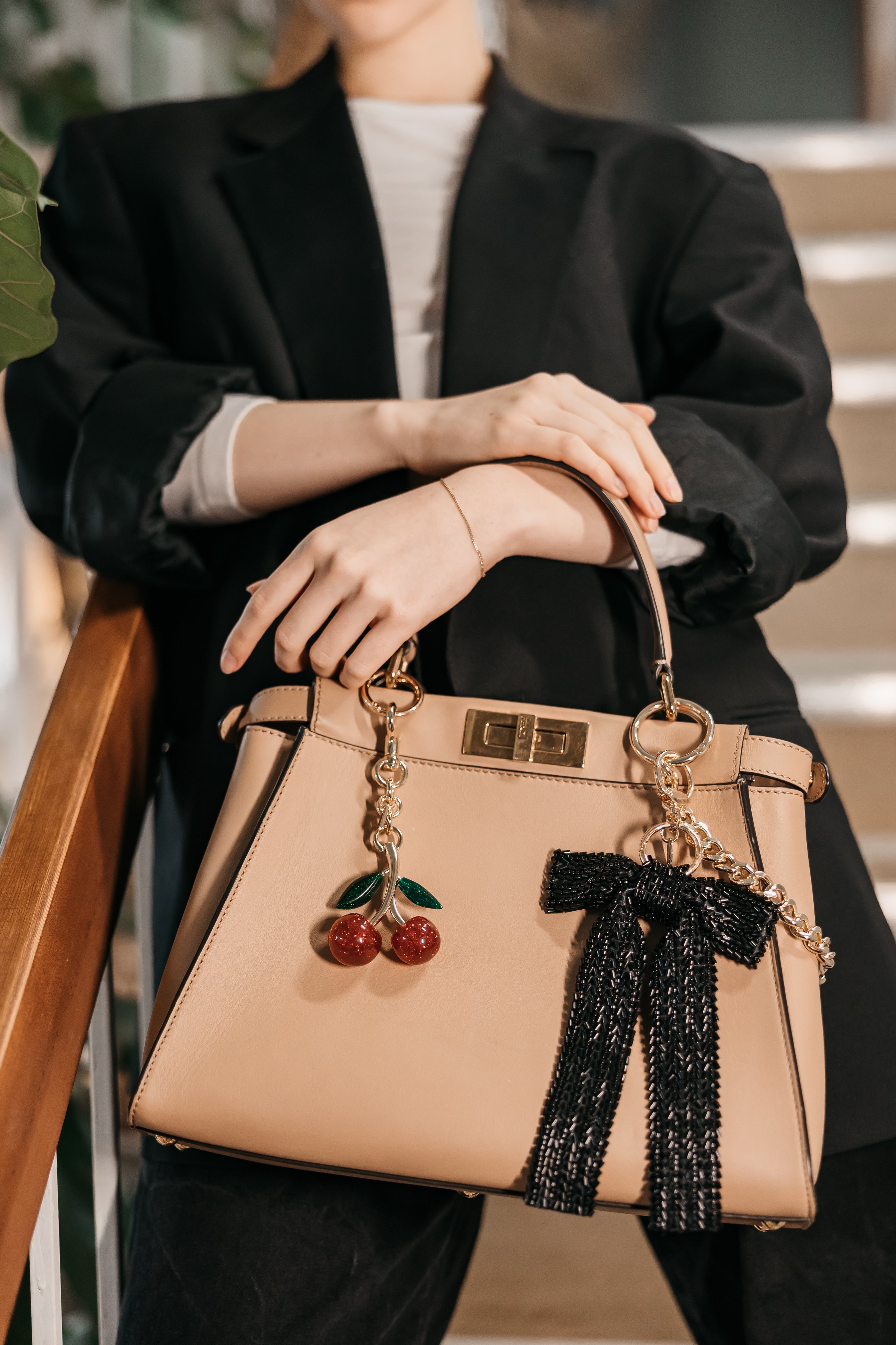 Person holding a beige handbag with purse charms, wearing a black blazer.