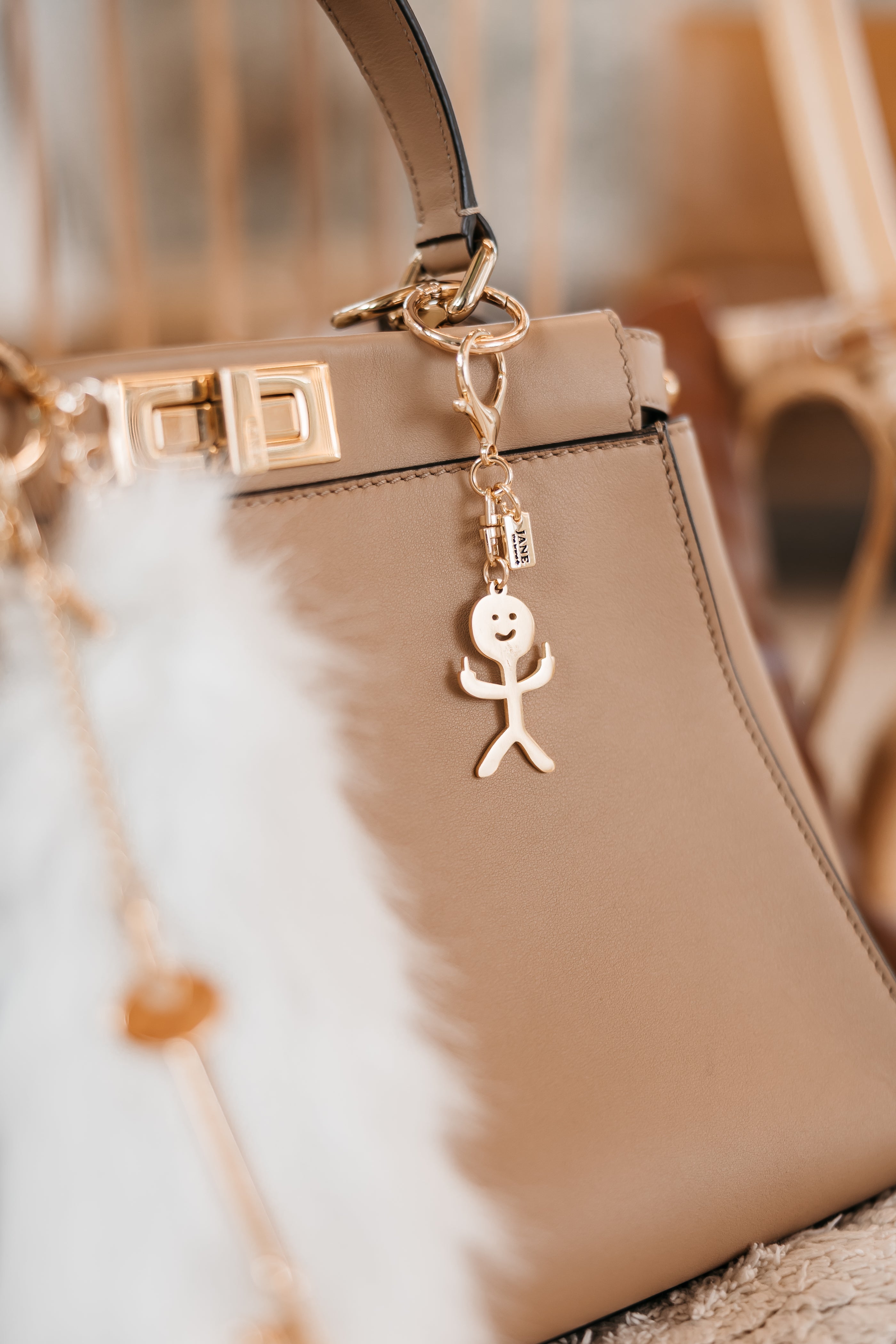 Beige handbag with a gold charm featuring a stick figure on a blurred background