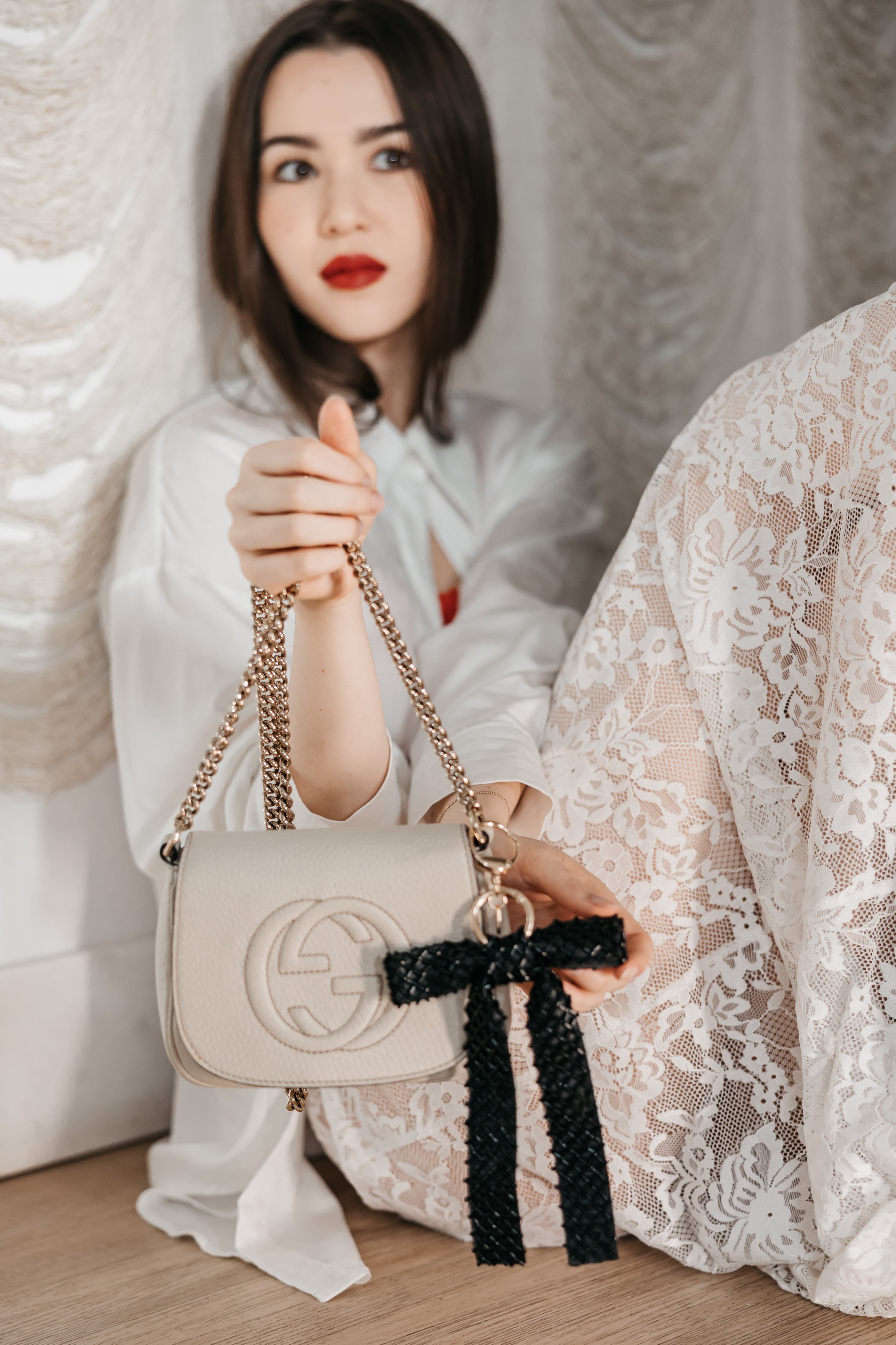 Woman holding a beige handbag with a black bow charm in a white room