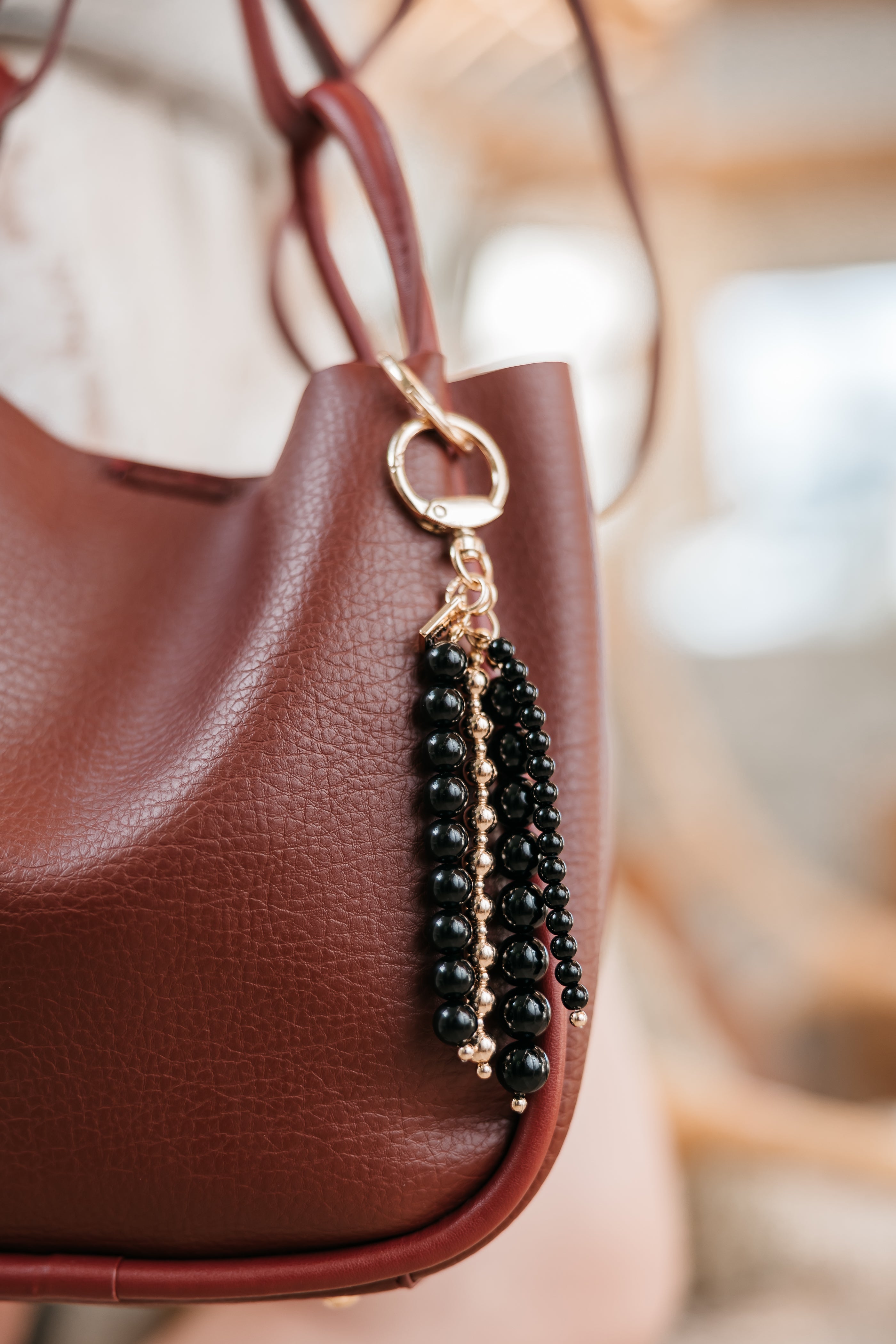 Black beaded charm attached to a brown leather handbag with a blurred background