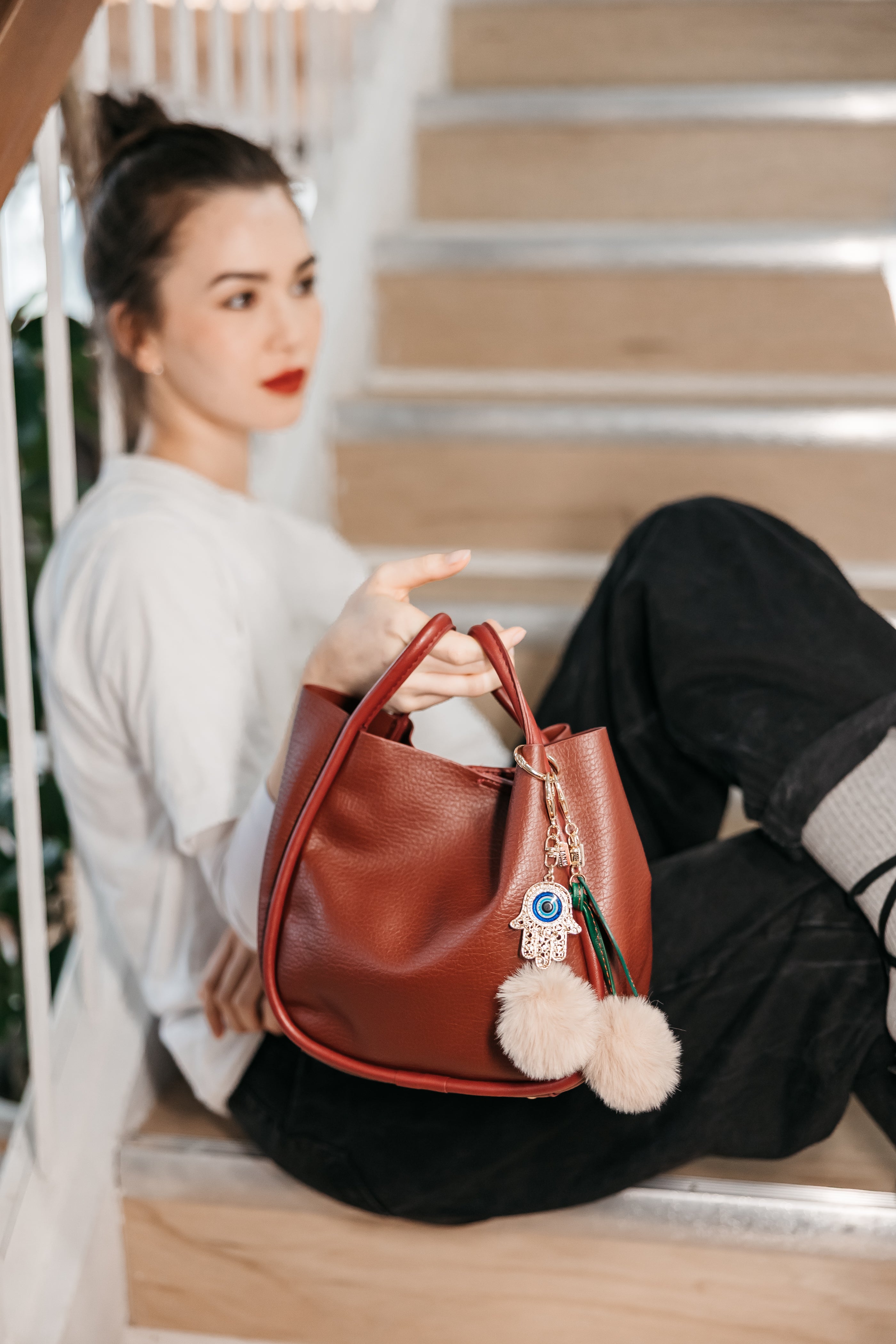 Woman holding a brown leather handbag with pom-pom charms details on a staircase.