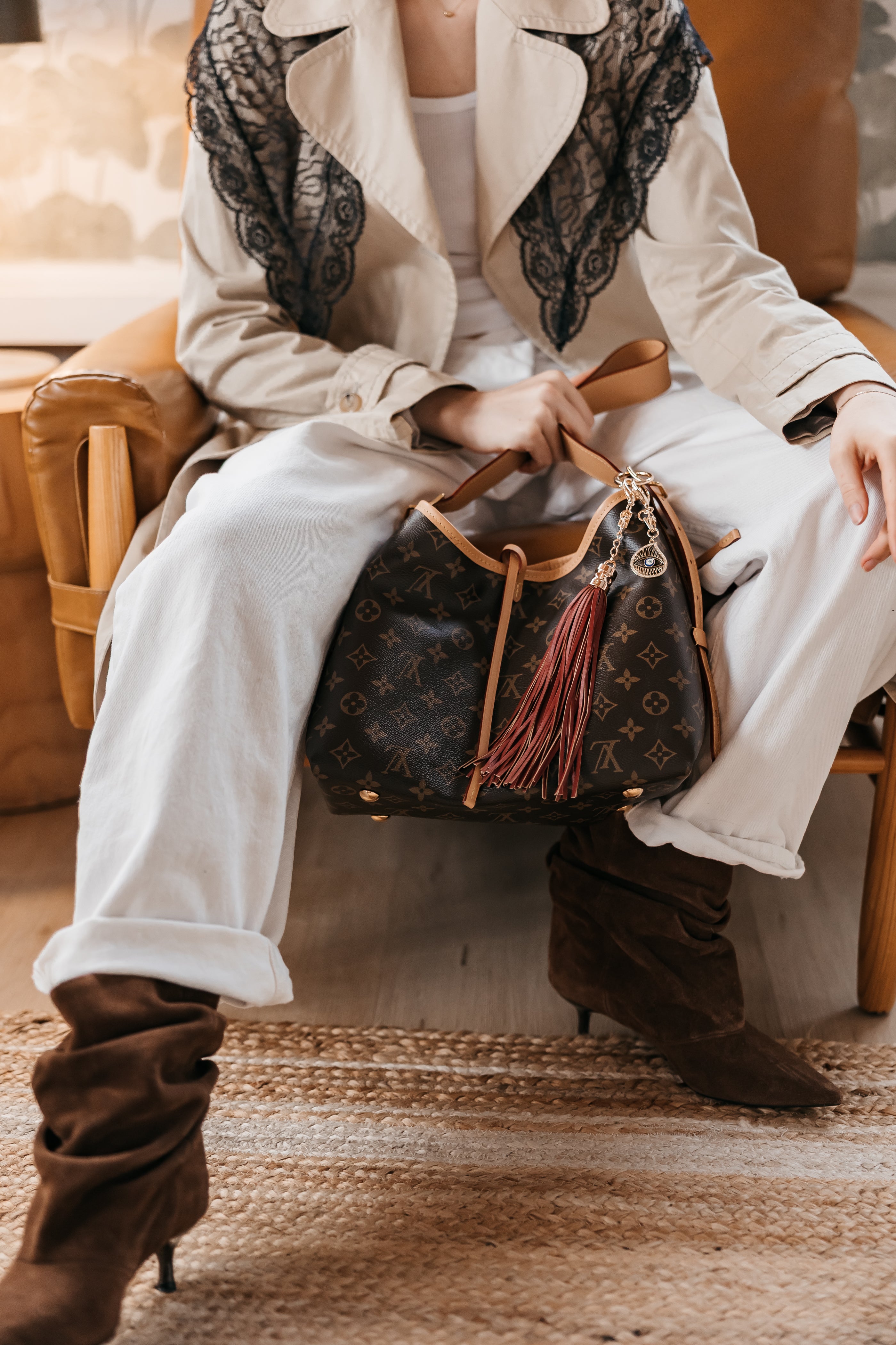 Person sitting on a chair holding a purse with charms wearing a white coat and brown boots.