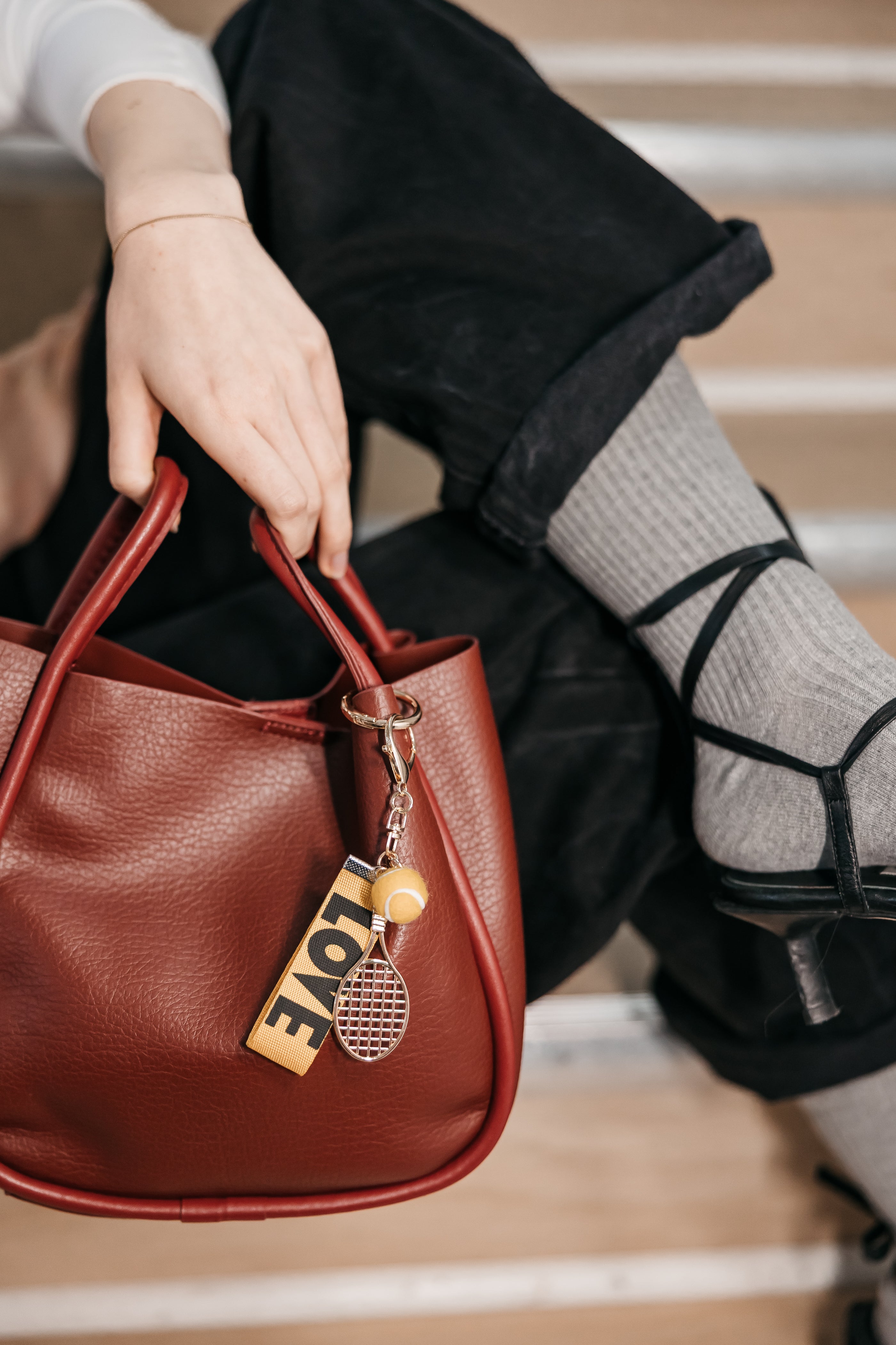 Person holding a brown handbag with a 'LOVE' charm on a neutral background
