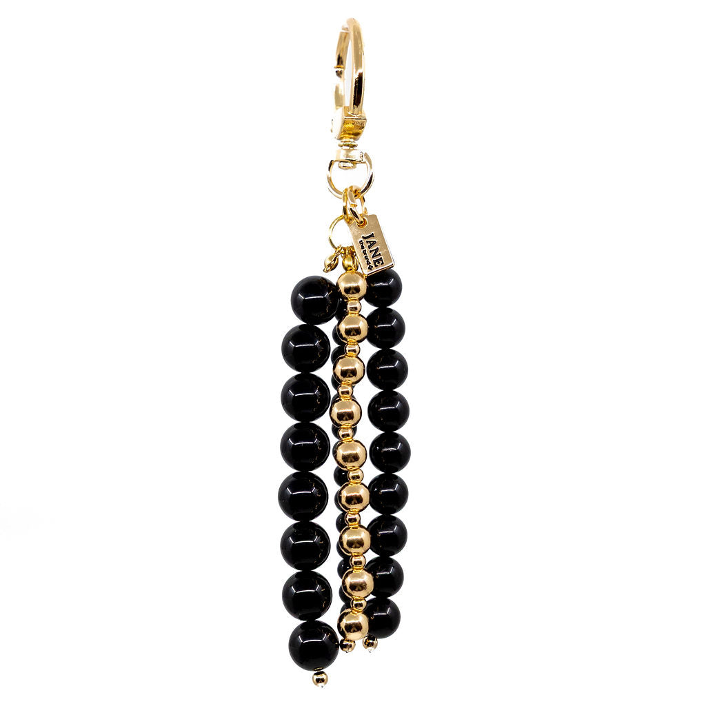 Black and gold Noir beaded bag charm hanging from a handbag.