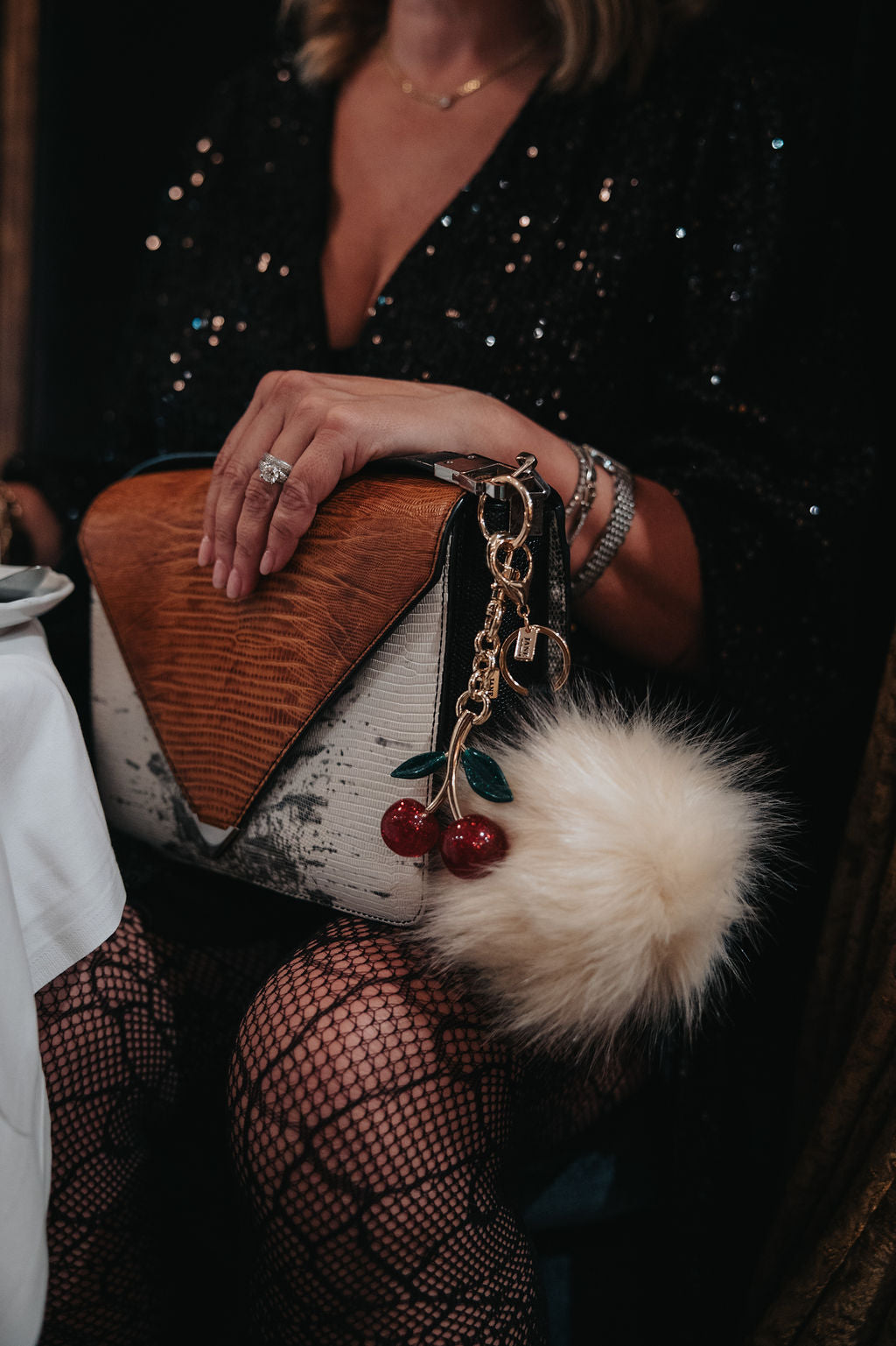 Person holding a handbag with a fur pom-pom and cherry charm.