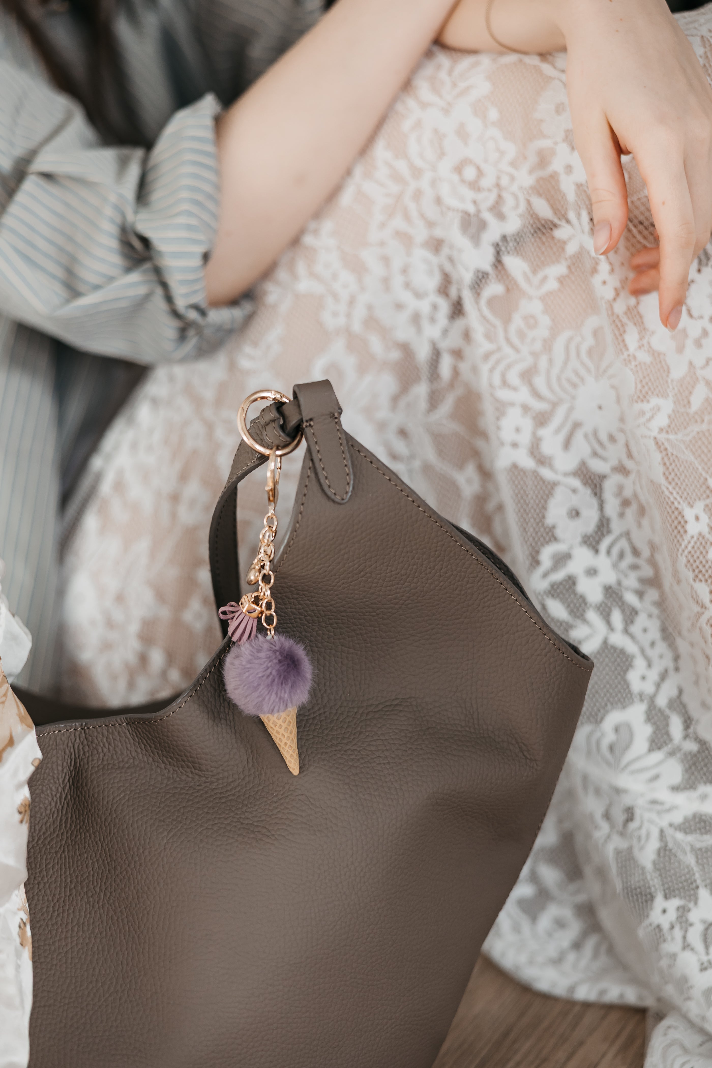 Brown handbag with a ice cream charm held by a person wearing a lace dress.