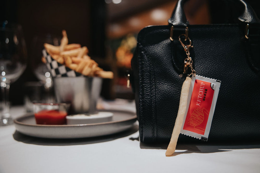 Black handbag with charm on a table setting with food and drinks.