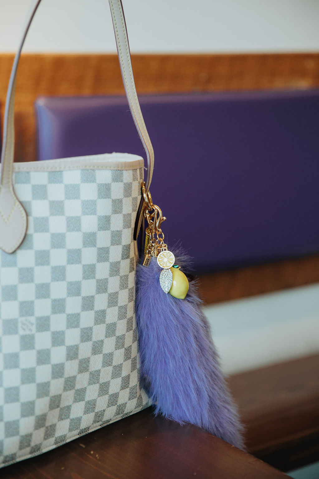 Checkered handbag with a purple tail charm and lemon charm on a wooden surface