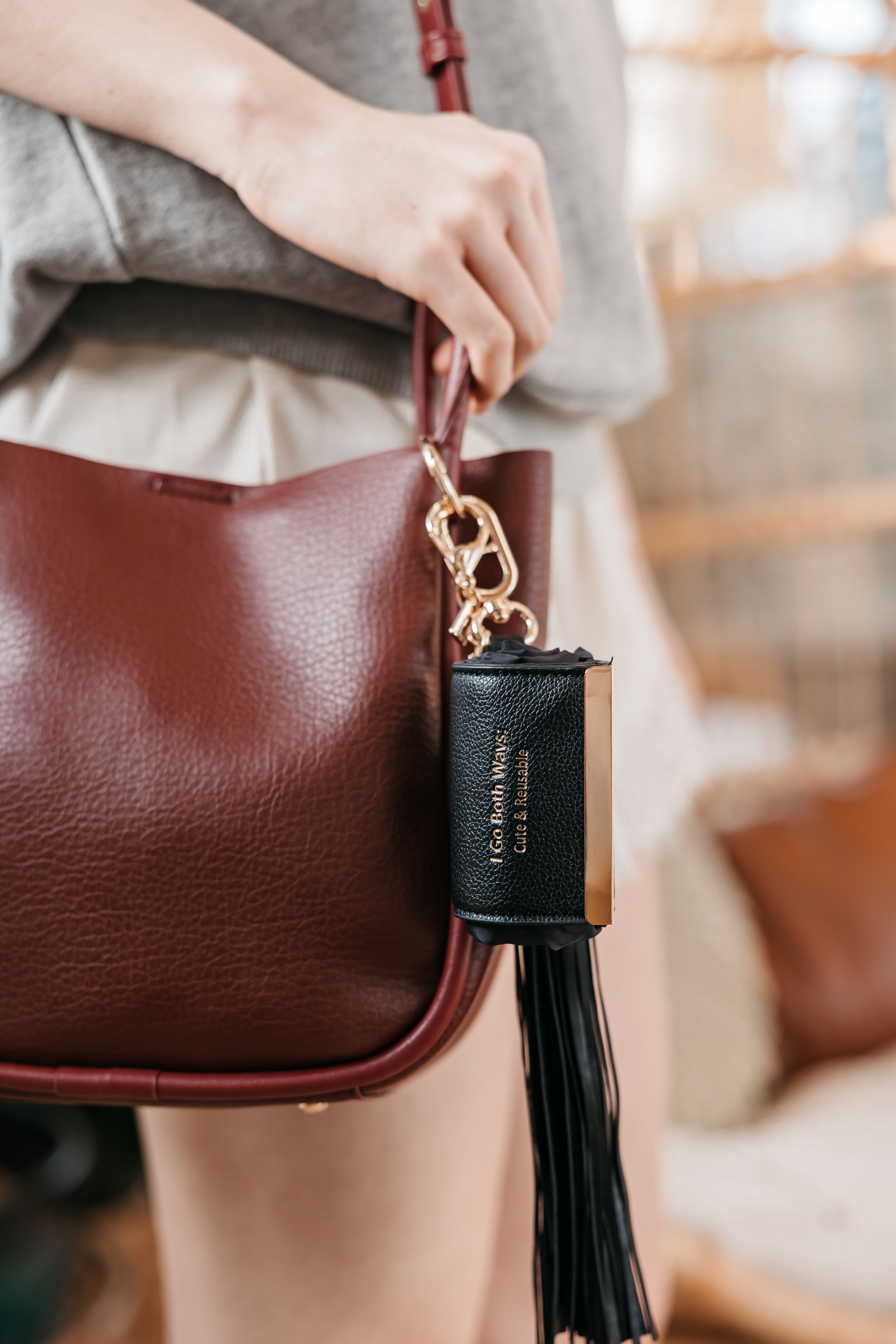 Brown leather handbag with a black tassel charm held by a person.