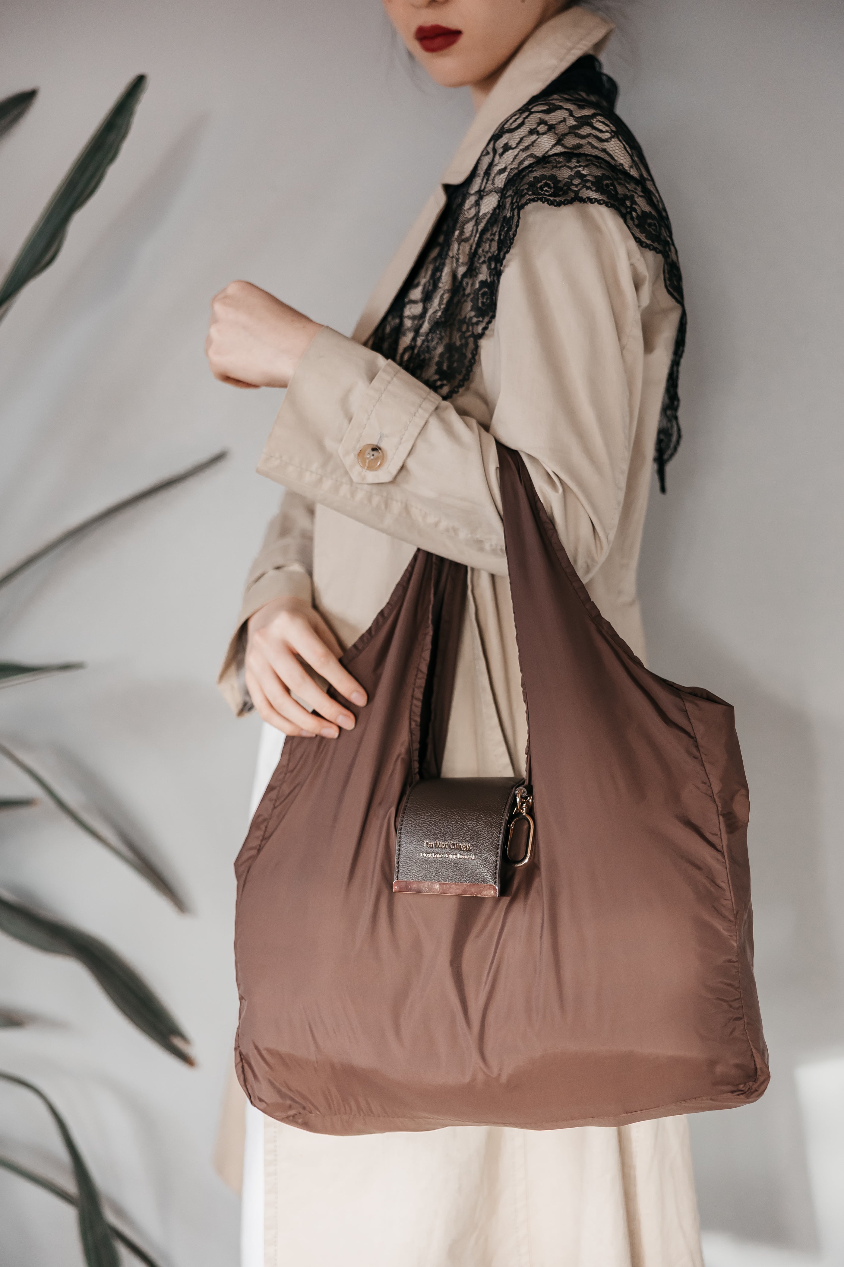 Person holding a brown tote bag with a neutral background reusable market bag chocolate brown. charm bag charm