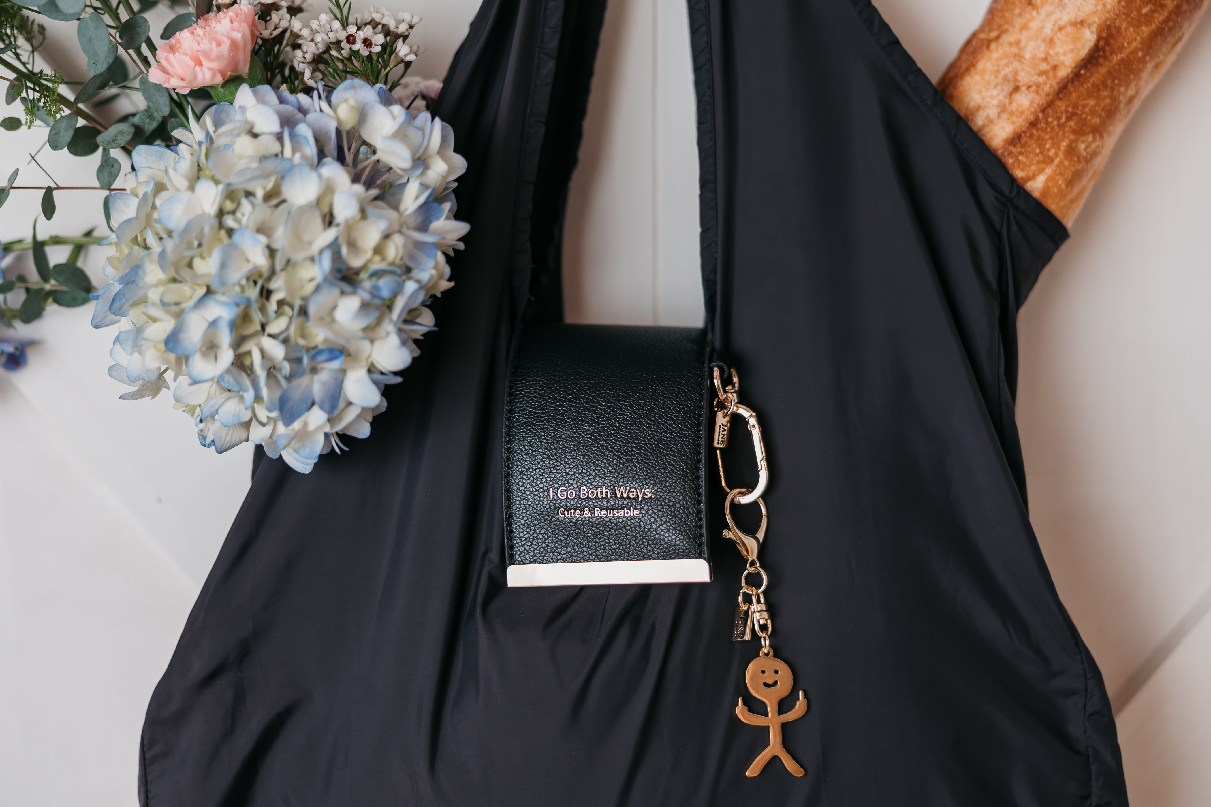Black sleeve with a notebook, keychain, and flowers on a light surface