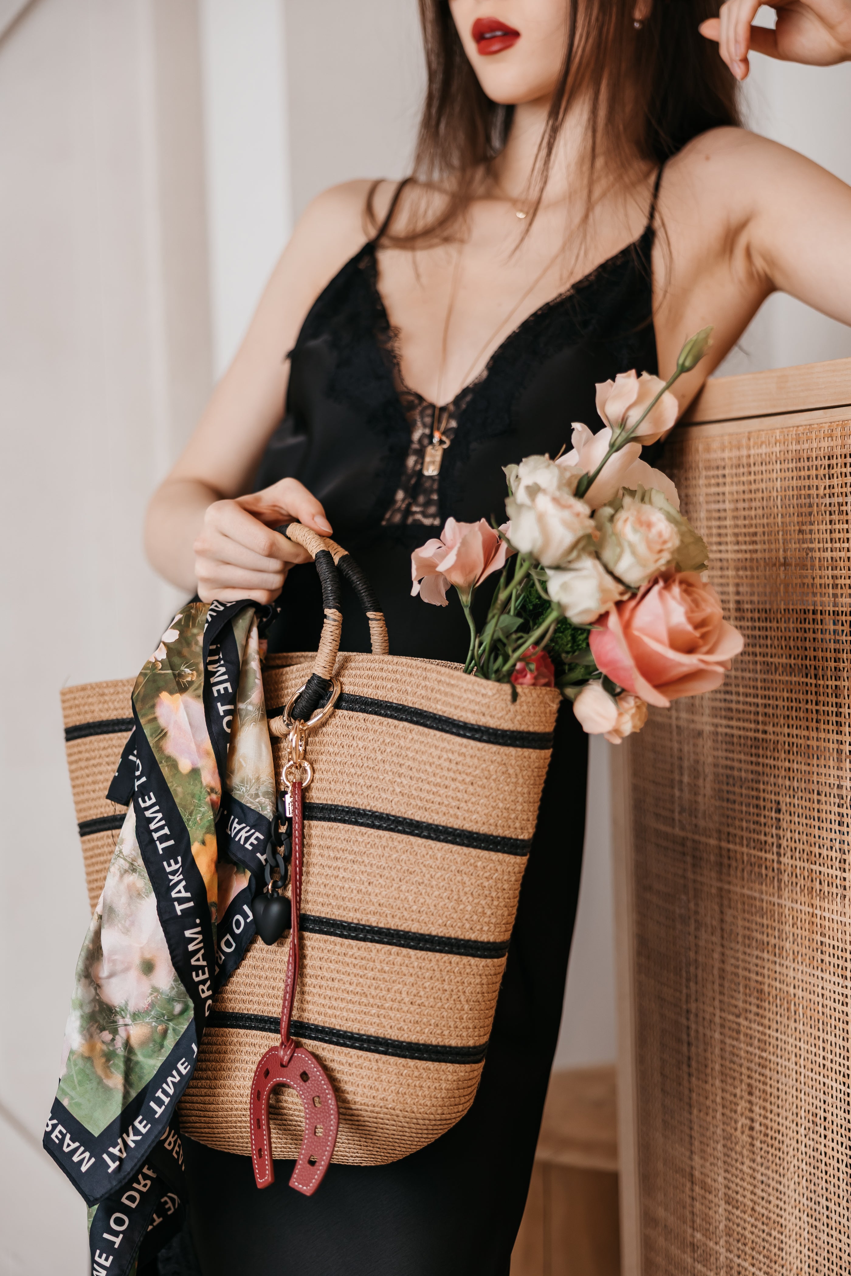 Woman holding a straw bag with floral accents and a bag charms wearing a black top.