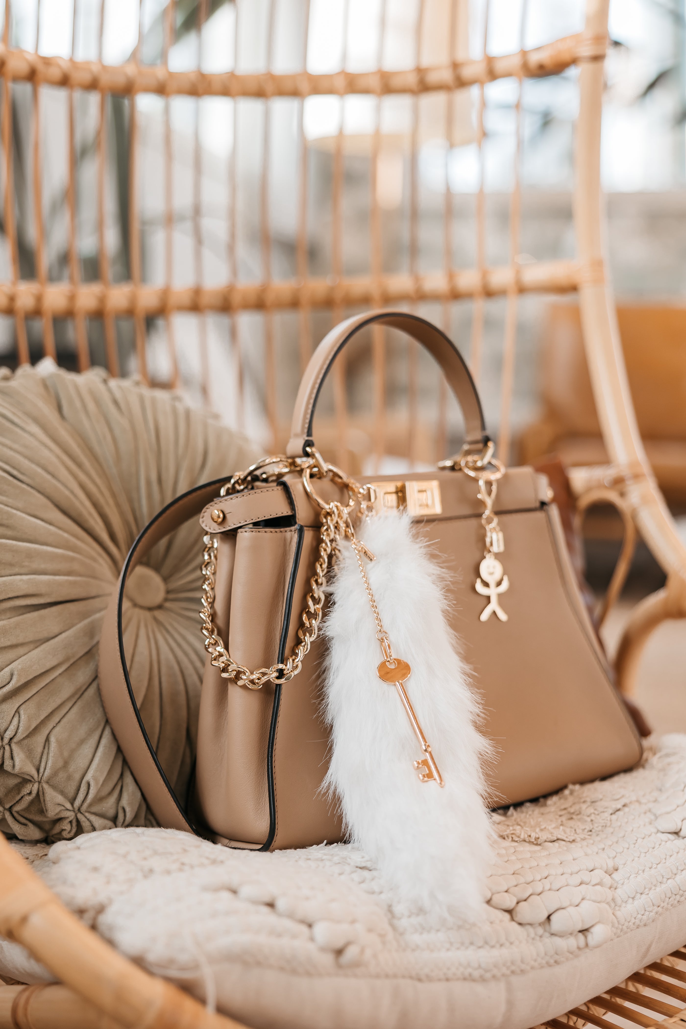 Beige handbag with decorative keychain charms on a textured surface